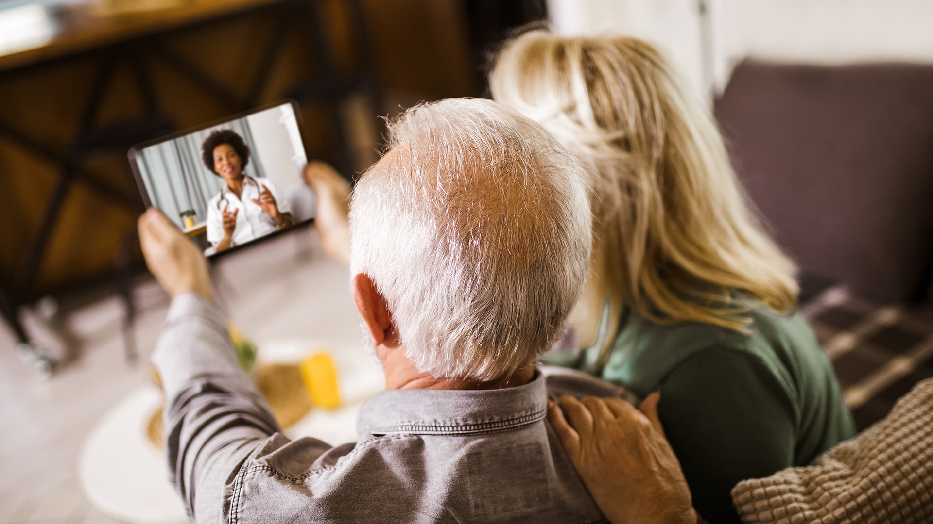 Senior couple at home holding digital tablet during video call with family doctor